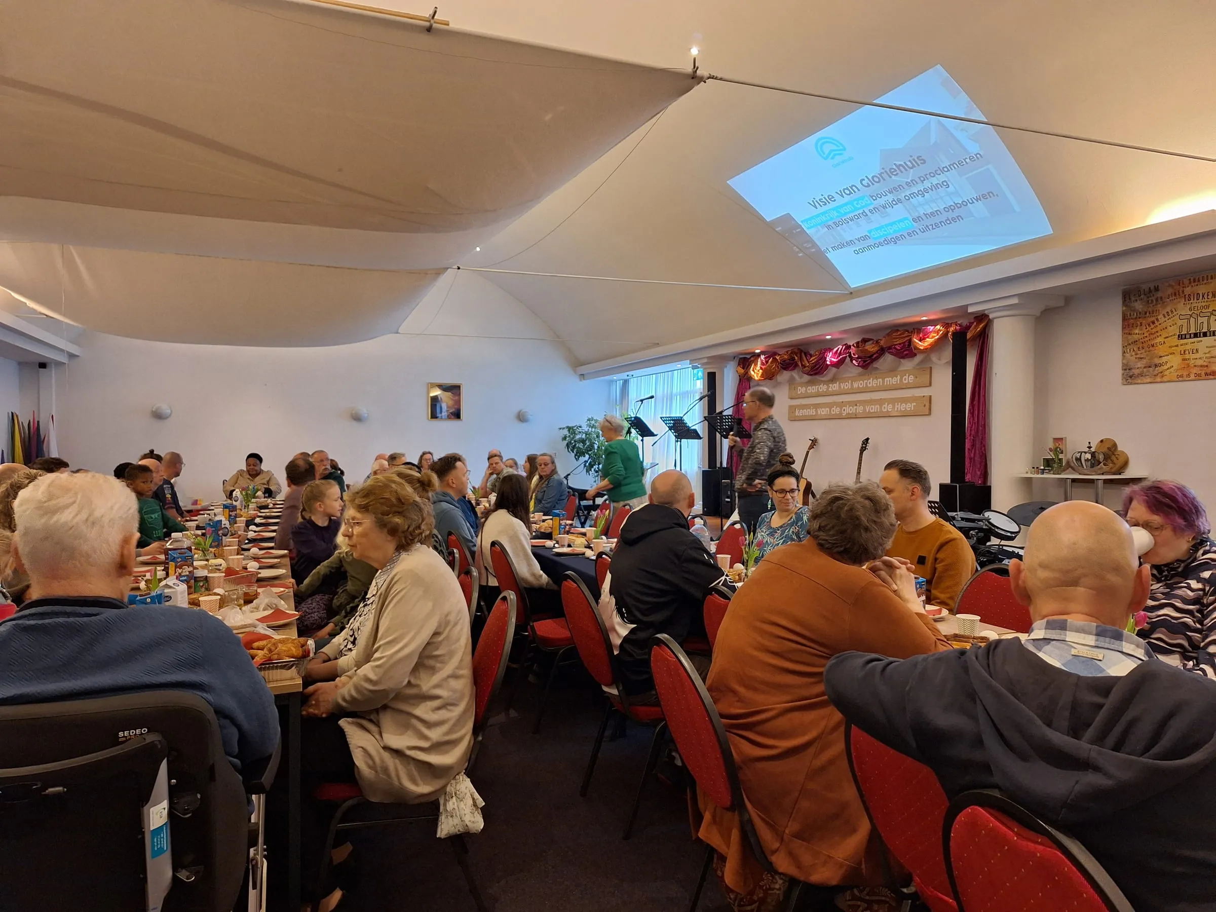 Een volle zaal met gemeenteleden aan lange tafels tijdens de paasmaaltijd